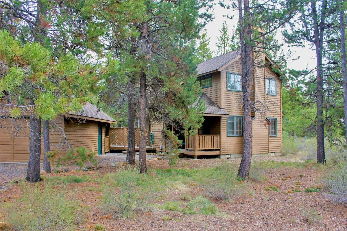 A wide exterior view capturing the two-story wooden house with a spacious deck and lush trees all around. The deck area is visible as a hub for outdoor activities and peaceful moments, echoing a sense of retreat and privacy.