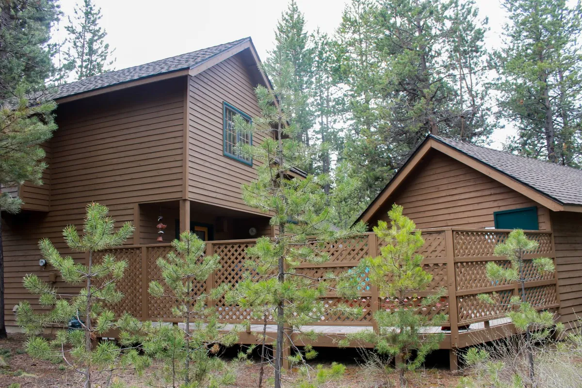 A cozy wooden deck nestled among trees, with charming architectural details and ample space for gatherings. The scene suggests a peaceful environment for morning coffee, barbecues, or simply enjoying nature from the comfort of the deck.