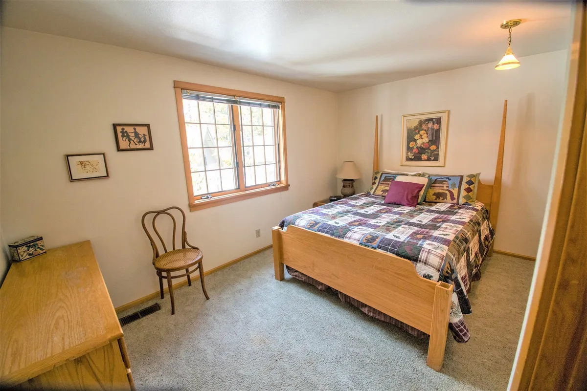 A calm bedroom with a queen bed, large window letting in natural light, a chair for reading or relaxing, and artwork that adds a touch of style. The space feels private and restful, ideal for couples or parents seeking a peaceful retreat.
