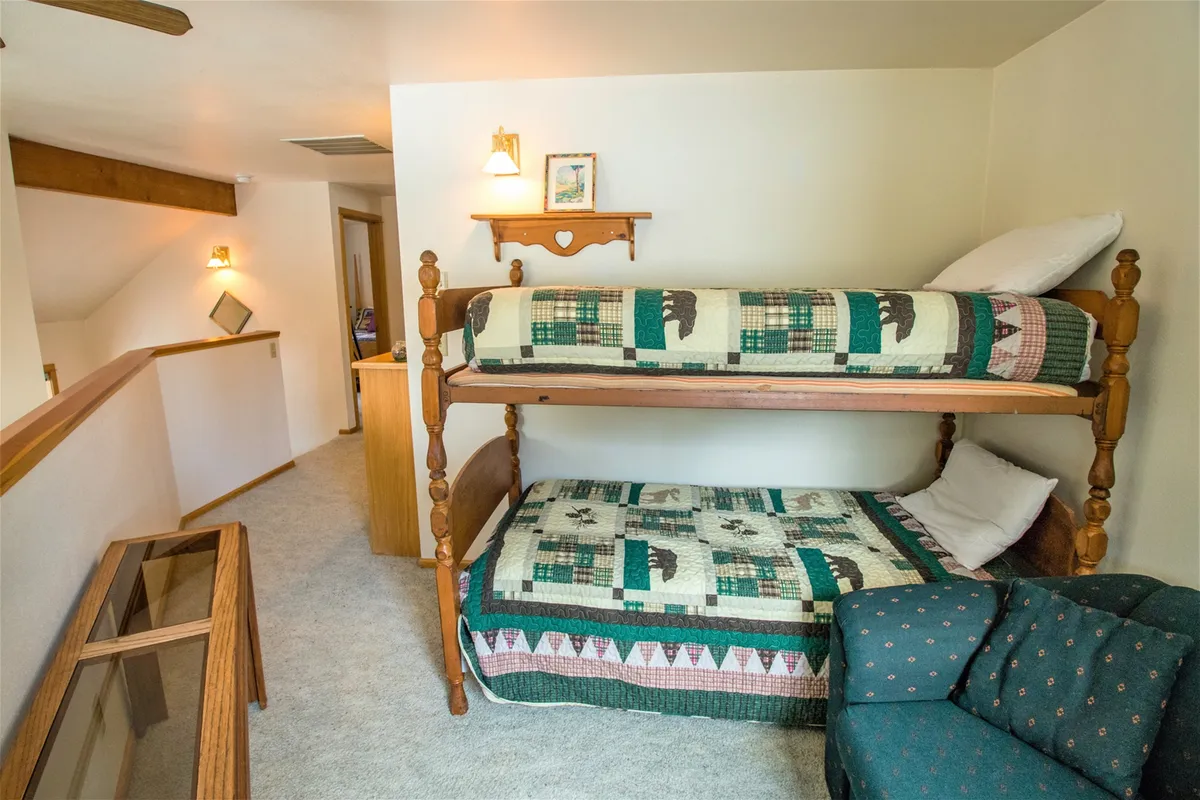 A playful and flexible loft space with sturdy bunk beds, a sofa for lounging or reading, and wall décor that adds a whimsical touch. The open layout invites sleepovers, storytelling, or relaxing downtime, making it ideal for kids or extra guests.
