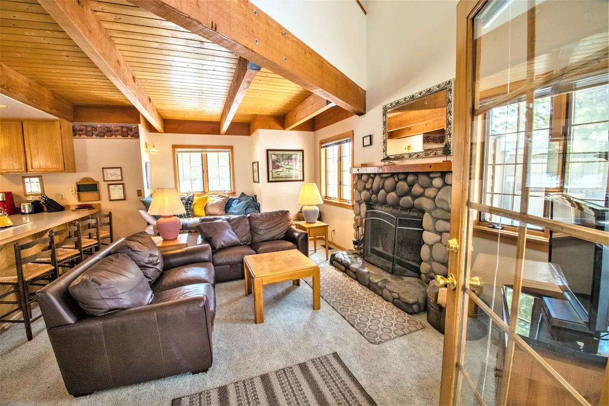 Featuring a welcoming living area with a soft leather sofa, prominent fireplace, and rustic wooden beams overhead. The space is styled for comfort, ideal for curling up with a book or enjoying lively conversation. A central coffee table invites group activities or casual snacks during movie nights.