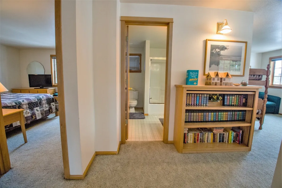 A cozy bedroom nook with a plush bed, bookshelf, and artwork, adjacent to a bathroom entrance. The scene suggests a quiet place to read, relax, or enjoy a private morning before heading out for the day's adventures.